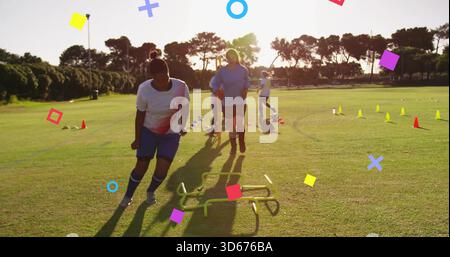 Trainiere Frauen in weißen Trikots, blauen Shorts, die bei Sonnenuntergang mit Kegeln auf dem Gras auf niedrigen Hürden navigieren Stockfoto