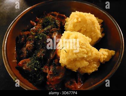 Mariniertes gebackenes Schweinefleisch mit Spinat serviert mit Butterpüree in traditioneller Tonplatte (traditionelles rumänisches Gericht) Stockfoto