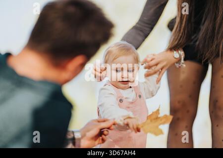 Die Familie genießt einen verspielten Moment im Herbstpark mit einem Baby, das lernt, Blätter zu ergreifen Stockfoto