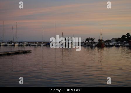 Ruhende Boote im Jachthafen Krk vor dem Pier, was das Bild mit rosa Wolken am Himmel und ihren Reflexen auf dem Wasser schneidet Stockfoto