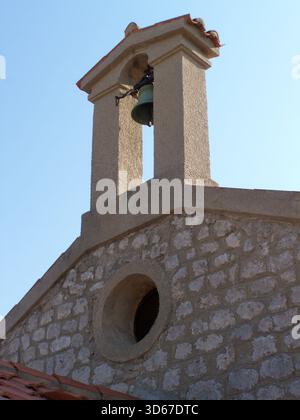 Kleiner offener Glockenturm im mediterranen Stil auf dem westlichen Giebel einer Kirche über einem runden Fenster Stockfoto