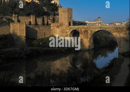 Römische und mittelalterliche Puente de Alcántara oder Alcántara-Brücke, die sich im ruhigen Fluss Tejo unter der UNESCO-Weltkulturerbestätte Toledo, Kastilien-La Mancha, Zentralspanien, spiegelt. Erbaut für das römische Municipium von Toletum, von den Westgoten genutzt und von den Mauren wiederaufgebaut, mit dem Westtor-Turm mit königlichen Wappen der spanischen katholischen Monarchen aus dem 15. Jahrhundert, Ferdinand und Isabella. Stockfoto