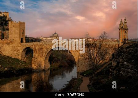 Wiederaufgebaute römische Puente de Alcántara oder Alcántara-Brücke, die sich im Fluss Tejo bei Toledo in Castilla-La Mancha, Zentralspanien, spiegelt. Sechseckiger Westtorturm aus dem 13. Jahrhundert, versetzt durch barocken Triumphbogen von 1721 (rechts, am anderen Ende der Brücke). Stockfoto