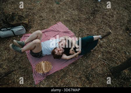 Ein Paar genießt ein Picknick im Freien auf einer rot-weiß karierten Decke im Wald Stockfoto