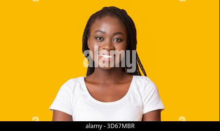 Junge lächelnde afrikanische amerikanische Frau auf gelbem Hintergrund Stockfoto