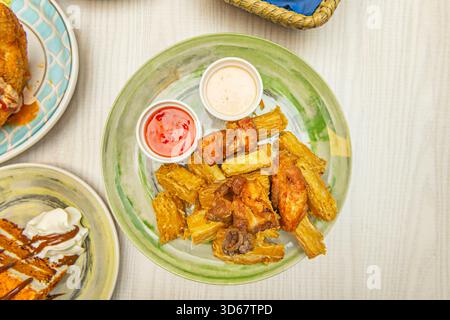 Karibische Art gebratener Yuca mit einer kreolischen Mojo-Sauce aus saurer Orange, Knoblauch und eingelegter roter Zwiebeln auf der Seite Stockfoto