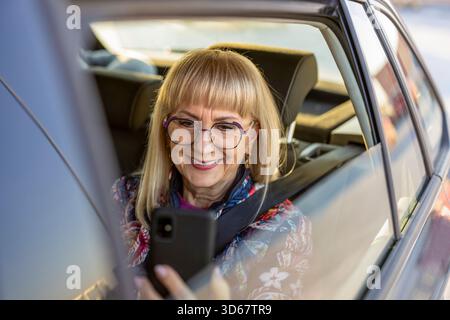Ältere Frau sitzt auf dem Rücksitz mit Smartphone Stockfoto