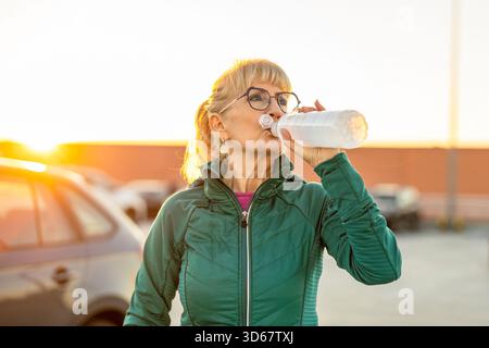 Reife Frau trinkt Wasser nach dem Training auf dem Parkplatz Stockfoto