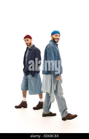 Zwei gutaussehende Brüder in trendiger Kleidung posieren selbstbewusst in einem hellen, künstlerischen Raum. Stockfoto