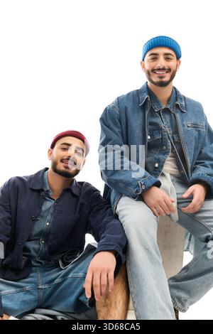 Zwei Zwillingsbrüder in stilvollen Outfits sitzen verspielt und zeigen ihren einzigartigen Sinn für Mode. Stockfoto