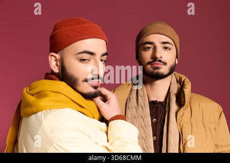 Zwei gutaussehende Zwillingsbrüder posieren selbstbewusst in stilvoller Kleidung vor farbenfroher Kulisse. Stockfoto