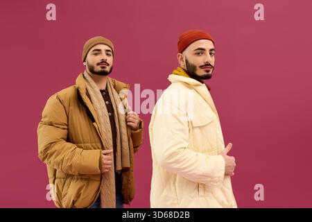 Zwei Brüder posieren selbstbewusst in modischen Outfits und betonen ihre auffällige Ähnlichkeit. Stockfoto