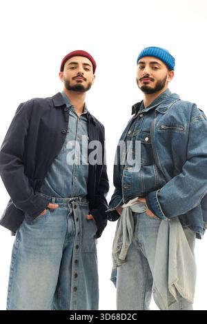 Zwei gutaussehende Zwillingsbrüder posieren selbstbewusst in stilvollen Outfits und bringen ihre Verbundenheit und ihr Flair zum Ausdruck. Stockfoto