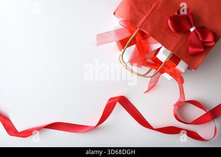 Konzept des Geschenks bei einer Feier mit einer roten Papiertasche mit Band gefüllt mit weißen Geschenkboxen mit rotem auf weißem Tisch mit wa Stockfoto