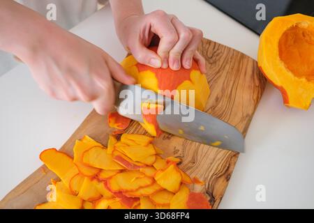 Eine Person schält vorsichtig einen Kürbis auf einem hölzernen Schneidebrett Stockfoto