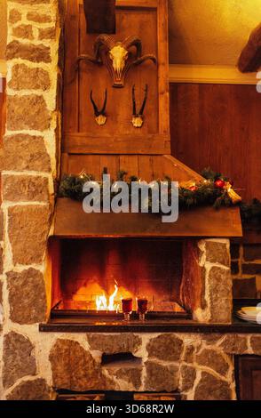Zwei Gläser mit Glühwein sind neben dem Kamin. Weihnachtsdekoration und Tassen mit einem scharfen Heißgetränk. Offene Feuer- und Steinmauern. Silvester Erholung, Entspannung und Urlaub Stockfoto