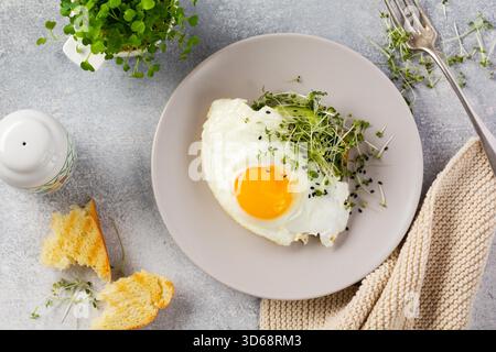 Traditionelles englisches Frühstück mit Spiegeleiern mit Rucola microgreen in grauer Keramikplatte auf grauem Beton altem Hintergrund. Draufsicht. Stockfoto