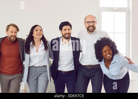 Energiegeladenes und zusammengeschlossenes multirassisches Geschäftsteam, das sich während der Pose im Büro breit lächelt. Stockfoto