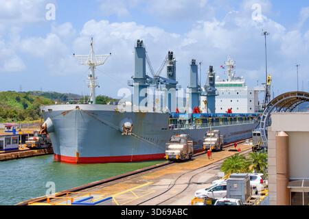 Großes Frachtschiff, das von speziellen Elektrolokomotiven im Panamakanal gezogen wird - Miraflores Schleusen vom Tribun des Besucherzentrums aus gesehen. Stockfoto