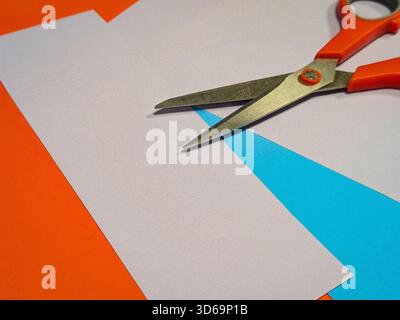 Überkopfaufnahme einer orangen Schere mit Griff auf lebendigem, geometrisch gefärbtem Papierhintergrund Stockfoto