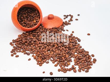 Kaffeebohnen, die aus rotem Keramikglas auf sauberem weißem Hintergrund verschüttet werden Stockfoto