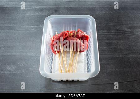 Blick auf einen Plastikbehälter mit eingelegtem Pfefferfleisch auf Spießen. Stockfoto