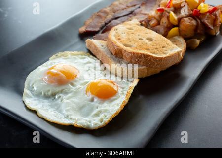 Blick auf einen Frühstücksteller mit Eiern, Toast, Speck und Kartoffeln. Stockfoto