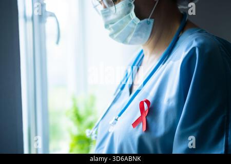 Medizinischer Fachmann mit rotem AIDS-Bewusstsein-Band auf Scheuern im Profil, Blick aus dem Fenster über HIV-Behandlung und -Pflege. Stockfoto