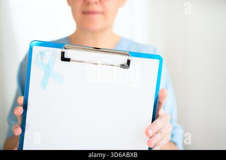 Nahaufnahme der Krankenschwester in medizinischer Kleidung mit blauem Band auf Uniform und Klemmbrett in den Händen. November Sensibilisierungsmonat für Prostatakrebs und Früherkennung Prävention. Stockfoto