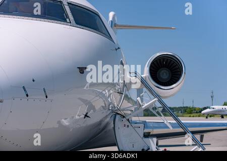 Nahaufnahme eines Geschäftsflugzeugs mit Turbofan-Motor, Rumpf, Cockpitfenstern und aufgesetzten Treppen. Flugzeug auf Asphalt mit Antenne V Stockfoto