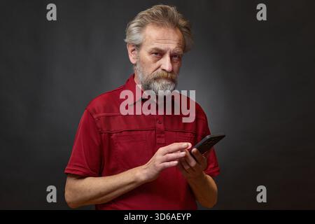Alter Mann über 60 Porträt im Studio mit Smartphone auf schwarzem Hintergrund Stockfoto