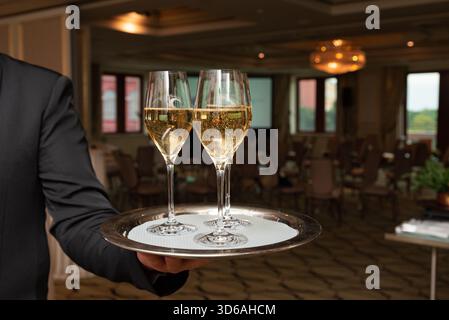 Zwei Sektgläser auf einem silbernen Tablett bilden den Rahmen für eine elegante Veranstaltung in einem stilvollen Bankettsaal. Die Umgebung ist perfekt für Hochzeiten, Feiern Stockfoto