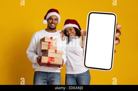 Glückliches Paar feiert Weihnachten mit Geschenken und Telefon vor gelbem Hintergrund Stockfoto