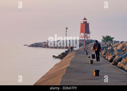 Der Leuchtturm am Racine North Pier und das rote Hafenlicht bei Sonnenaufgang mit rosafarbenem Nebel und einem Mann, der mitten im Sommer den Pier hinuntergeht. Stockfoto