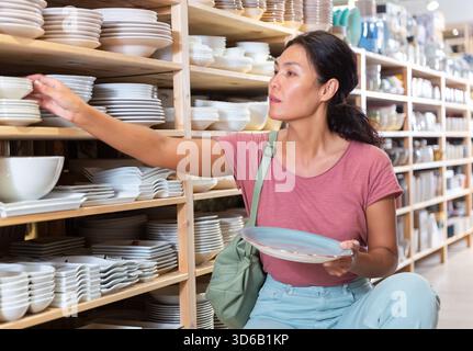 Positive weibliche Käufer wählt neue Teller im Geschirrladen Stockfoto
