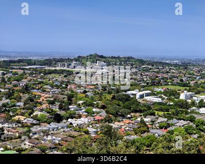 Breiter erhöhter Blick auf die Vororte von Auckland mit Wohnhäusern, Grünflächen und fernen Hügeln unter einem hellblauen Himmel. Stockfoto