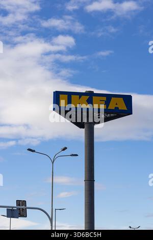 Hohes, dreieckiges IKEA-Schild mit markantem blau-gelbem Logo, auf einer grauen Säule, vor einem hellblauen Himmel mit fleckigen weißen Wolken Stockfoto