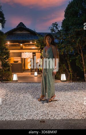 Frau am Machiya-Hauseingang in der Abenddämmerung in Kyoto mit leuchtenden Laternen Stockfoto