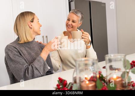 Mutter und Tochter in Strickpullis, die Keramikbecher mit zündeten Kerzen auf der Kücheninsel anschlagen Stockfoto