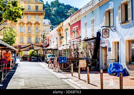Farbenfrohe enge Gassen und alte Gebäude in der historischen Altstadt von Nizza, Frankreich, mit Rollern, Cafés, Rollläden, und warmes mediterranes Licht. Stockfoto