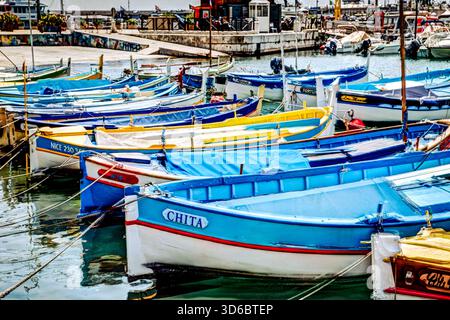 Farbenfrohe Fischerboote liegen im Hafen in der Nähe von Nizza, Frankreich, mit Gebäuden am Mittelmeer im Hintergrund. Stockfoto