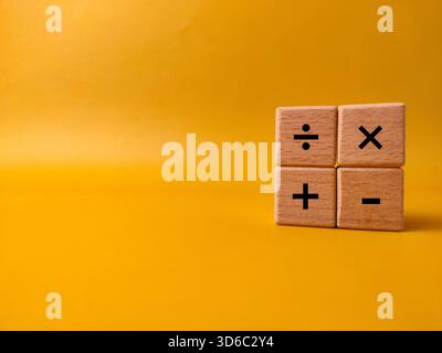 Das Bild zeigt vier Holzblöcke mit grundlegenden mathematischen Betriebssymbolen auf gelbem Hintergrund. Stockfoto