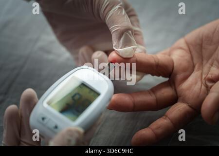 Schließen Sie einen Arzt mit Glukometer auf, der den Blutzuckerspiegel einer älteren Frau überprüft. Diabeteskonzept Stockfoto