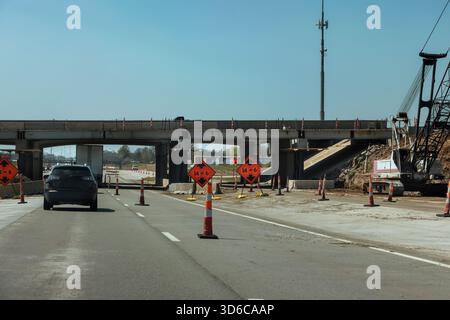 Fahrzeuge fahren durch Straßenbaugebiete, wobei Warnschilder für schwere Maschinen sichtbar sind. Stockfoto
