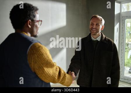 Kaukasischer Mann mittleren Alters schüttelt die Hände mit schwarzem Mann mittleren Alters drinnen Stockfoto