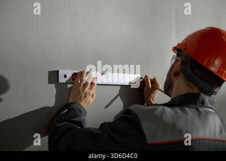 Kaukasischer Mann mittleren Alters, der während der Arbeit die Wand mit der Wasserwaage misst Stockfoto