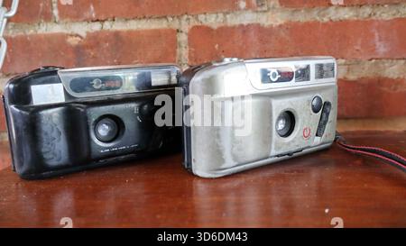 Machen Sie eine Nahaufnahme des alten Vintage Point und machen Sie Filmkameras mit integriertem Blitz auf einem Holztisch vor einer rustikalen Ziegelwand. Konzept der Retro-Fotografie Stockfoto