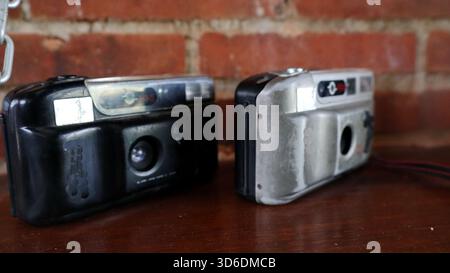 Machen Sie eine Nahaufnahme des alten Vintage Point und machen Sie Filmkameras mit integriertem Blitz auf einem Holztisch vor einer rustikalen Ziegelwand. Konzept der Retro-Fotografie Stockfoto