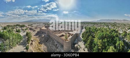 Aus der Vogelperspektive auf die alte Zitadelle von Arg-e Rayen, die in starkem Kontrast zu dem üppigen Grün steht, das sie umgibt, Rayen, Provinz Kerman, Iran. Stockfoto