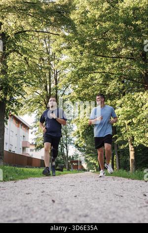 Zwei männliche Freunde joggen gern in einem Park, einer mit einer Beinprothese, und teilen sich einen motivierenden Moment im Freien. Stockfoto